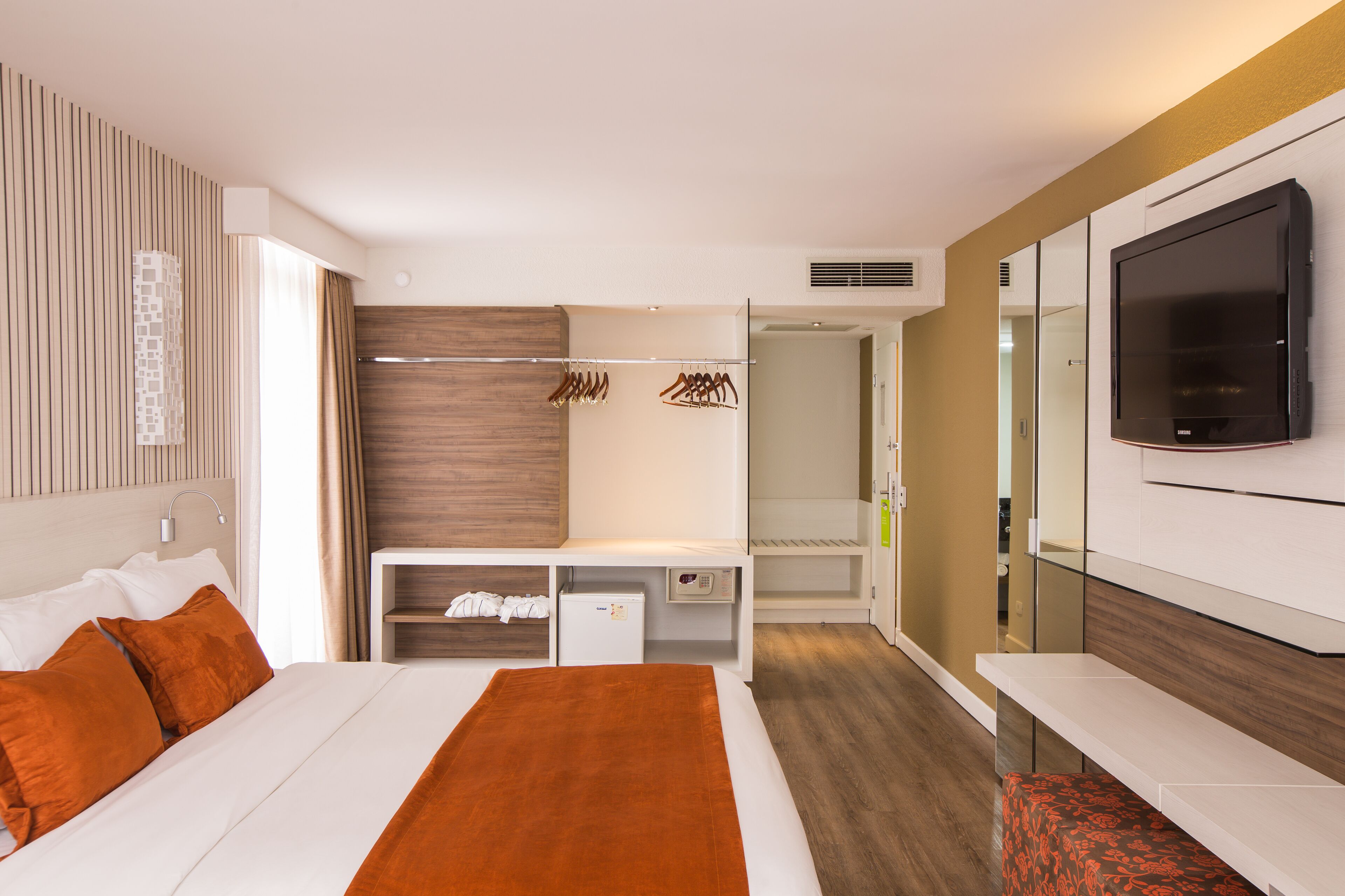 Quarto de hotel moderno com cama, televisão, guarda-roupa e secretária.