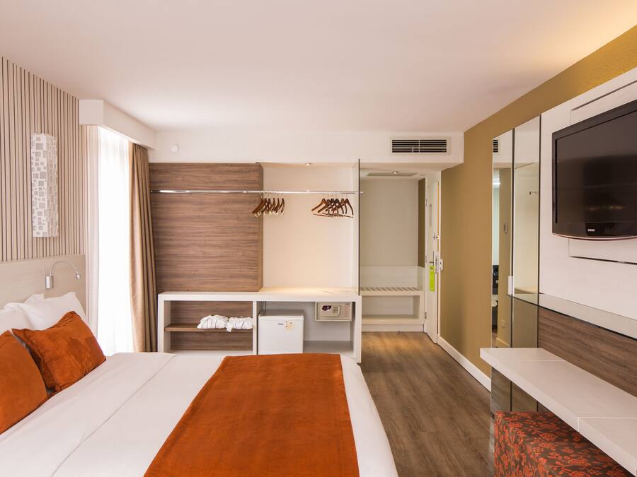 Quarto de hotel moderno com cama, televisão, guarda-roupa e secretária.