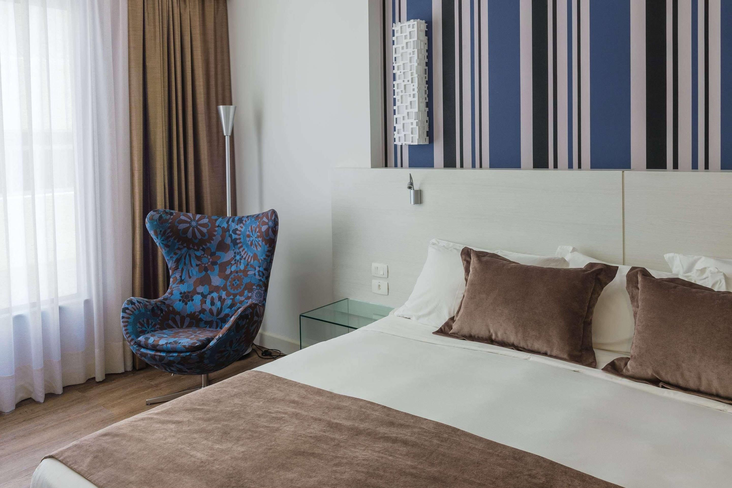 Una habitación de hotel con una cama, una silla, una mesita de noche y una pared decorada con rayas.