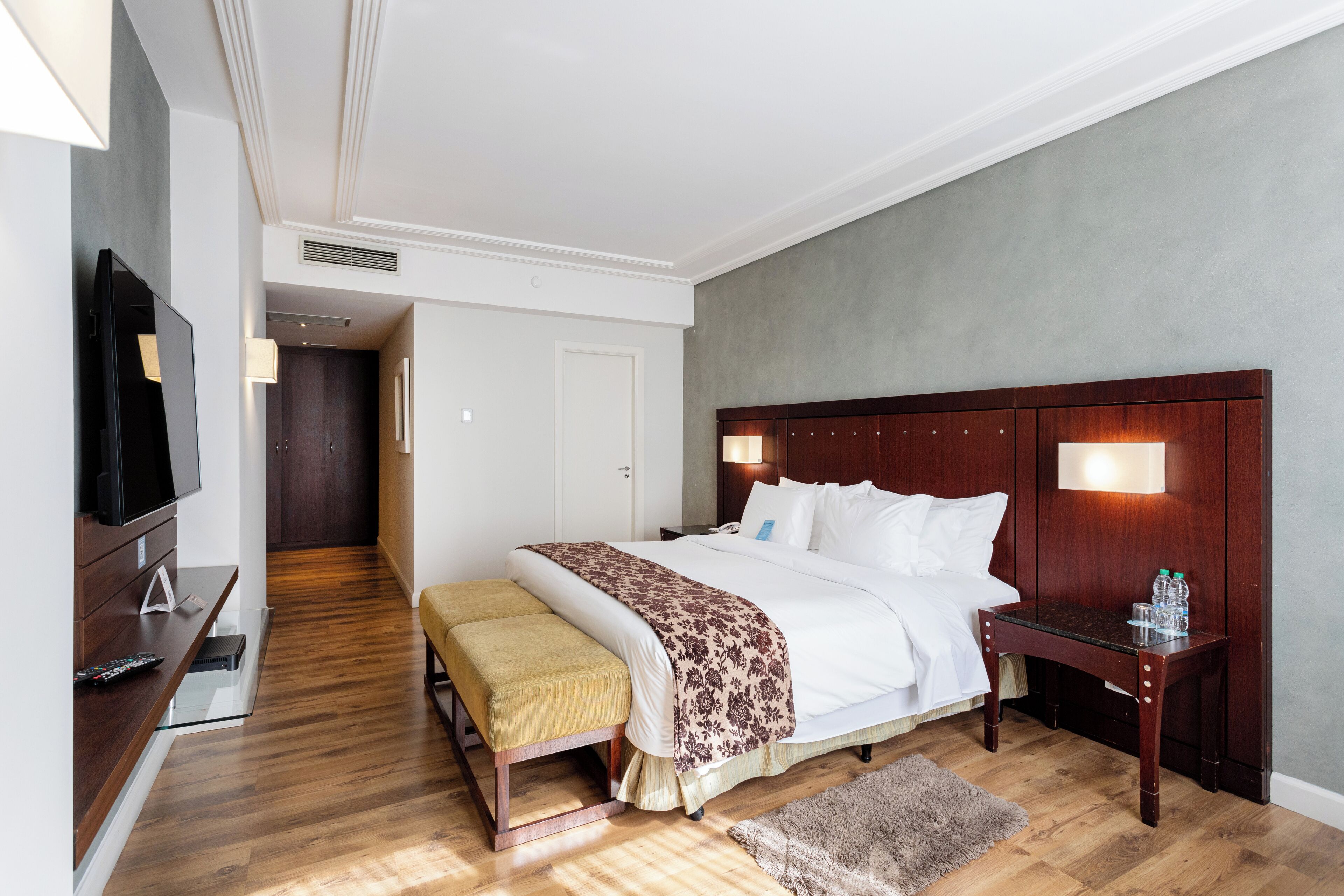 Habitación de hotel con una cama grande, mesitas de noche, televisión y suelo de madera.