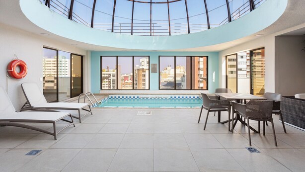 A rooftop pool area with lounge chairs, a table, and a glass ceiling. - Radisson Hotel Curitiba (Curitiba)