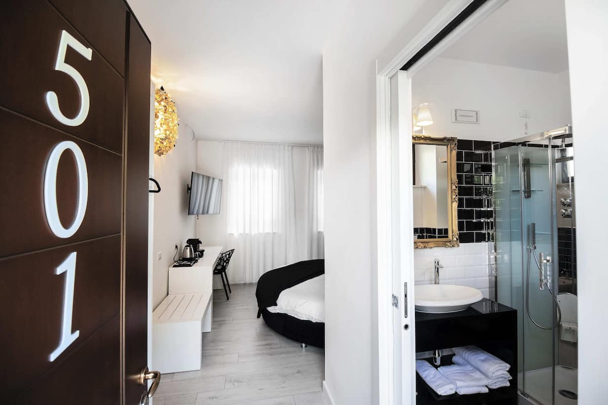 Ein modernes Hotelzimmer mit Bett, Schreibtisch, Stuhl und einem Badezimmer mit Duschkabine sowie einem großen Spiegel.
