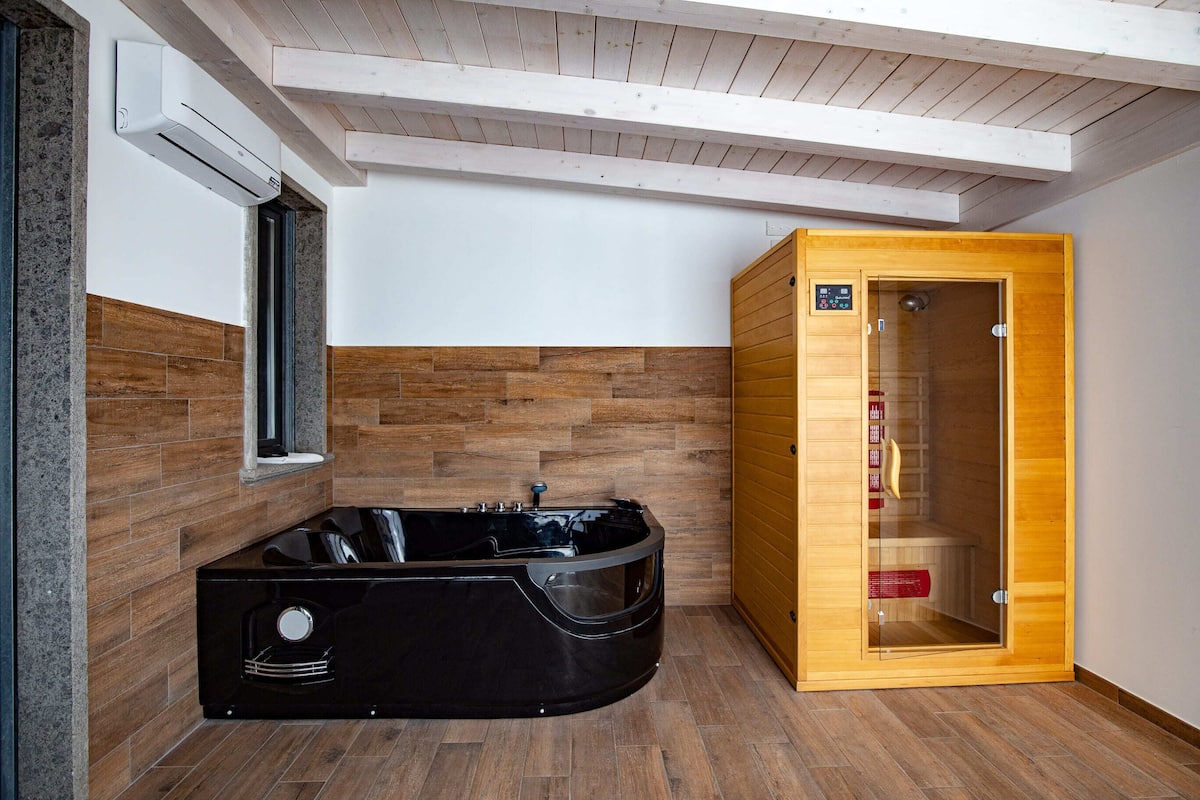 Ein modernes Badezimmer mit einer schwarzen Whirlwanne, einer Holzauna und einer Wand mit Steinplatten.
