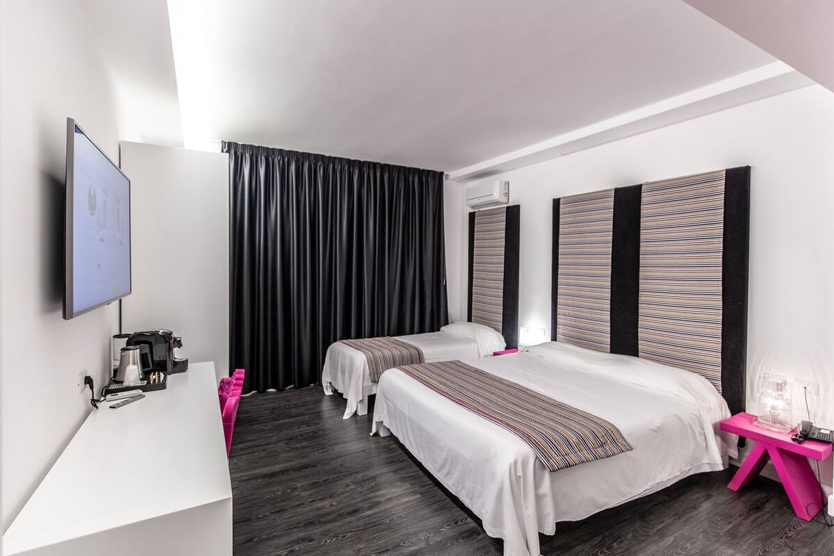 Ein modernes Hotelzimmer mit zwei Betten, einem Schreibtisch, einer Kaffeemaschine und einem Fernseher.
