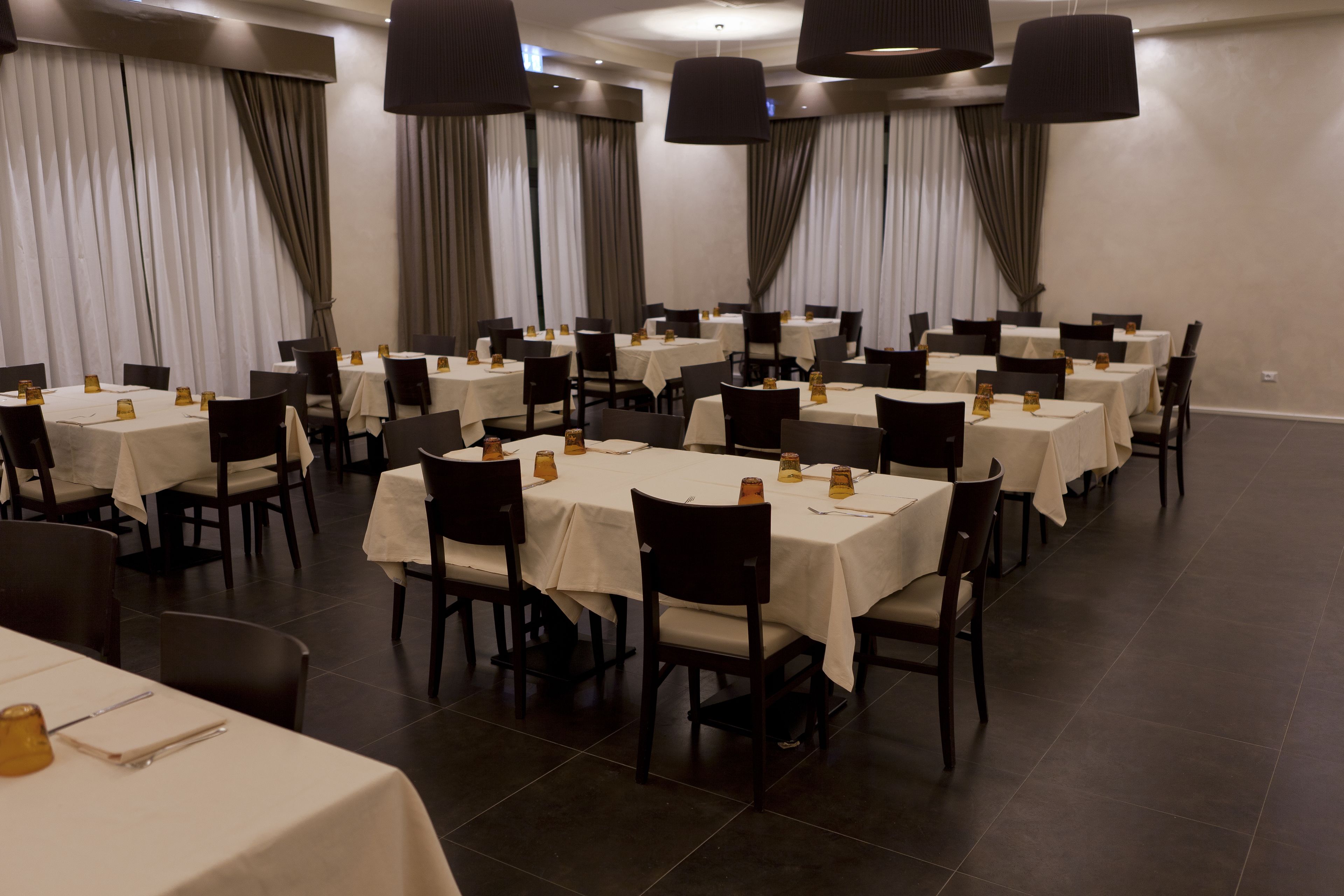 Een ruime eetzaal met meerdere tafels, stoelen en hangende lampen.
