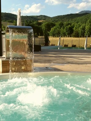 Un jacuzzi con cascada, rodeado por una piscina y vistas a un paisaje montañoso.
