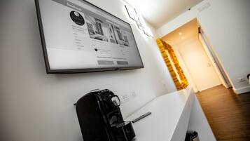A hotel room with a large flat-screen TV mounted on the wall displaying a Facebook page.