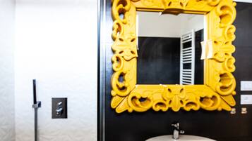 Un bagno con un lavandino bianco, uno specchio decorato giallo e un soffione.