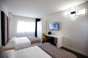 Habitación de hotel con dos camas, un escritorio, una silla, un televisor y una ventana con cortinas.