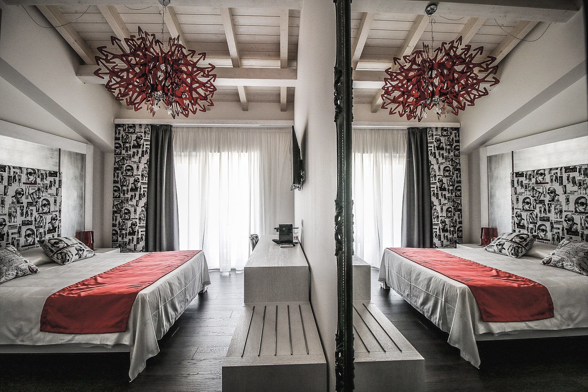 A mirrored room with two beds, a central table, and a large chandelier.