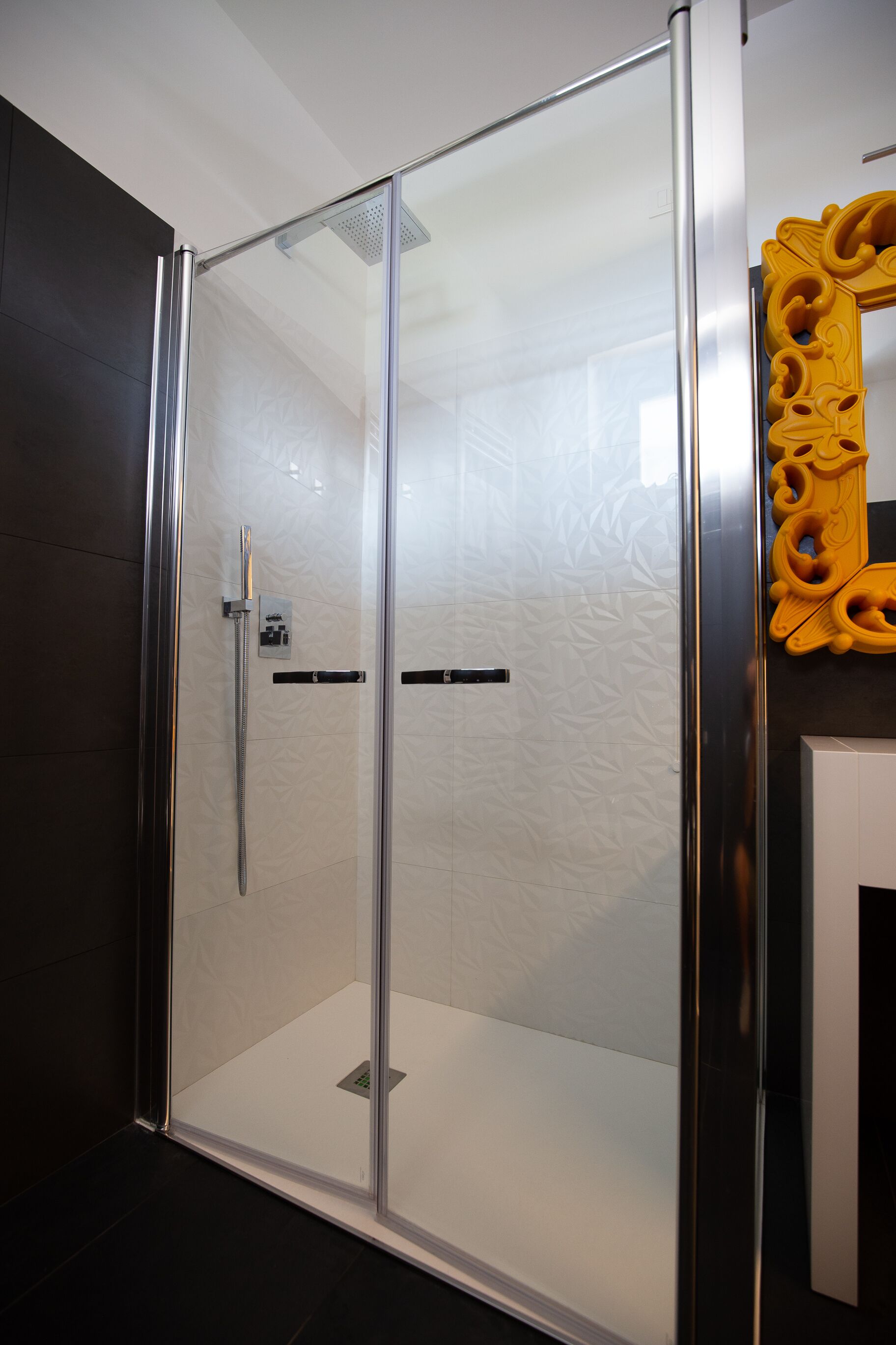 A modern bathroom with a glass-enclosed shower, a large mirror, and a dark floor.