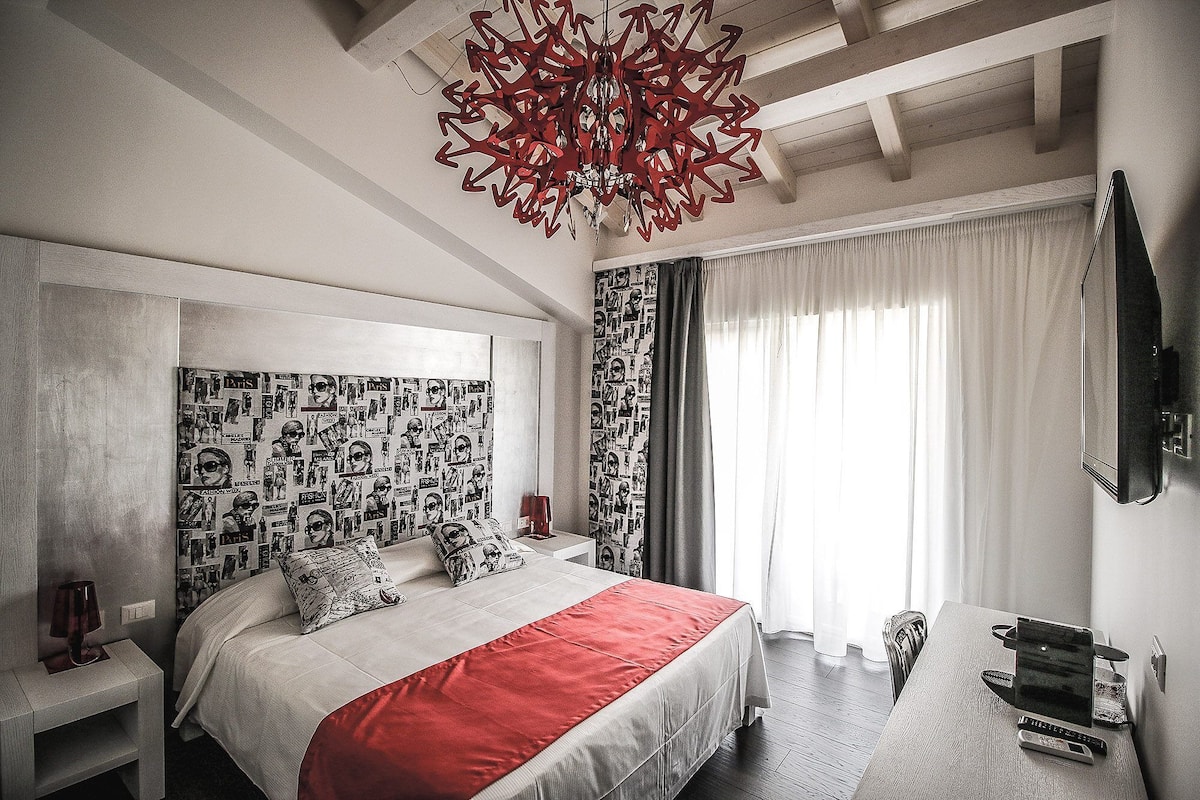 Ein Schlafzimmer mit Bett, roher Tagesdecke, einem gemusterten Kopfteil, einem Nachttisch, einem Schreibtisch und einem Fernseher.