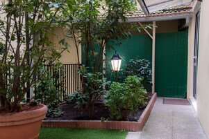 A courtyard with a potted plant, a small garden bed, a green door, and a lamp post.
