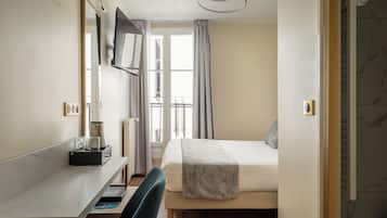 Une chambre d’hôtel comprenant un lit, un bureau avec une chaise, un téléviseur fixé au mur et une fenêtre avec des rideaux.