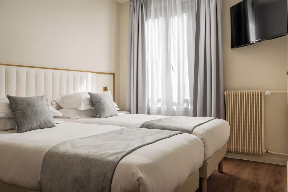 Ett hotellrum med två sängar, en platt-TV som är monterad på väggen och ett fönster med gardiner.