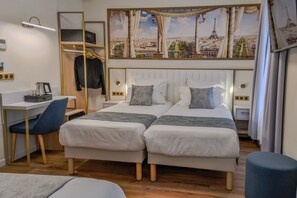 Habitación de hotel con dos camas, un escritorio, una silla, un armario y un mural grande con un paisaje urbano en la pared.