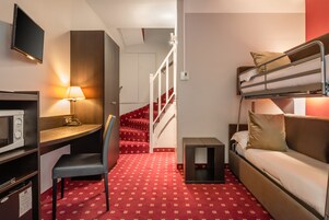 A compact hotel room with a bunk bed, a desk with a lamp, a microwave, and a small table.