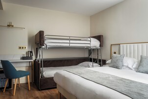 Una camera d'albergo con un letto a castello, una scrivania con una sedia e un letto con cuscini.