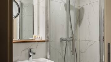 Een moderne badkamer met een douchecabine van glas, een wand betegeld met wit marmer, een wastafel met chromen kraan en een spiegel boven de wastafel.