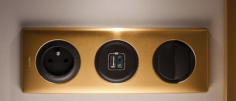 Toma de corriente empotrada en la pared con tres enchufes, incluyendo un puerto USB, sobre un panel dorado.
