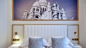 Habitación de hotel con una gran foto enmarco de un edificio histórico, una cama blanca con dos almohadas y lámparas de noche.