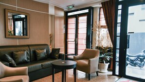 Una sala de estar moderna con un sofá de cuero, una mesa redonda y un sillón de cuero. Hay un espejo grande en la pared, una planta en maceta y una puerta que da al exterior.