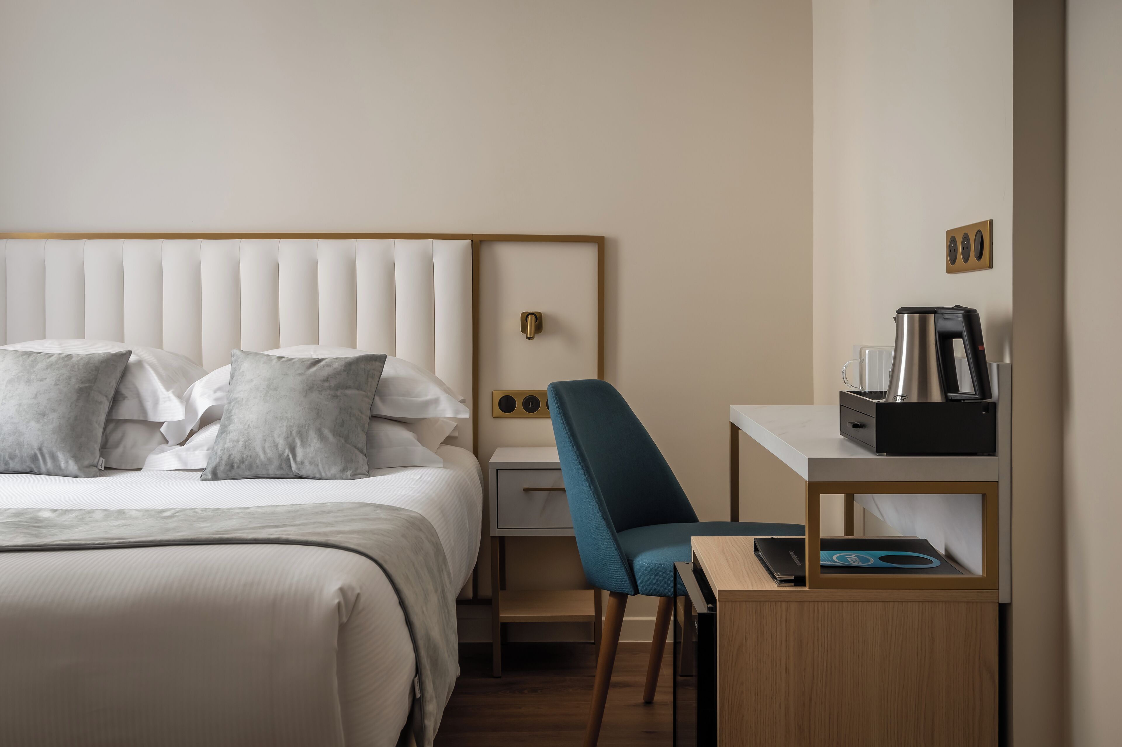 A hotel room with a bed, a desk, a chair, a nightstand, and a coffee maker.