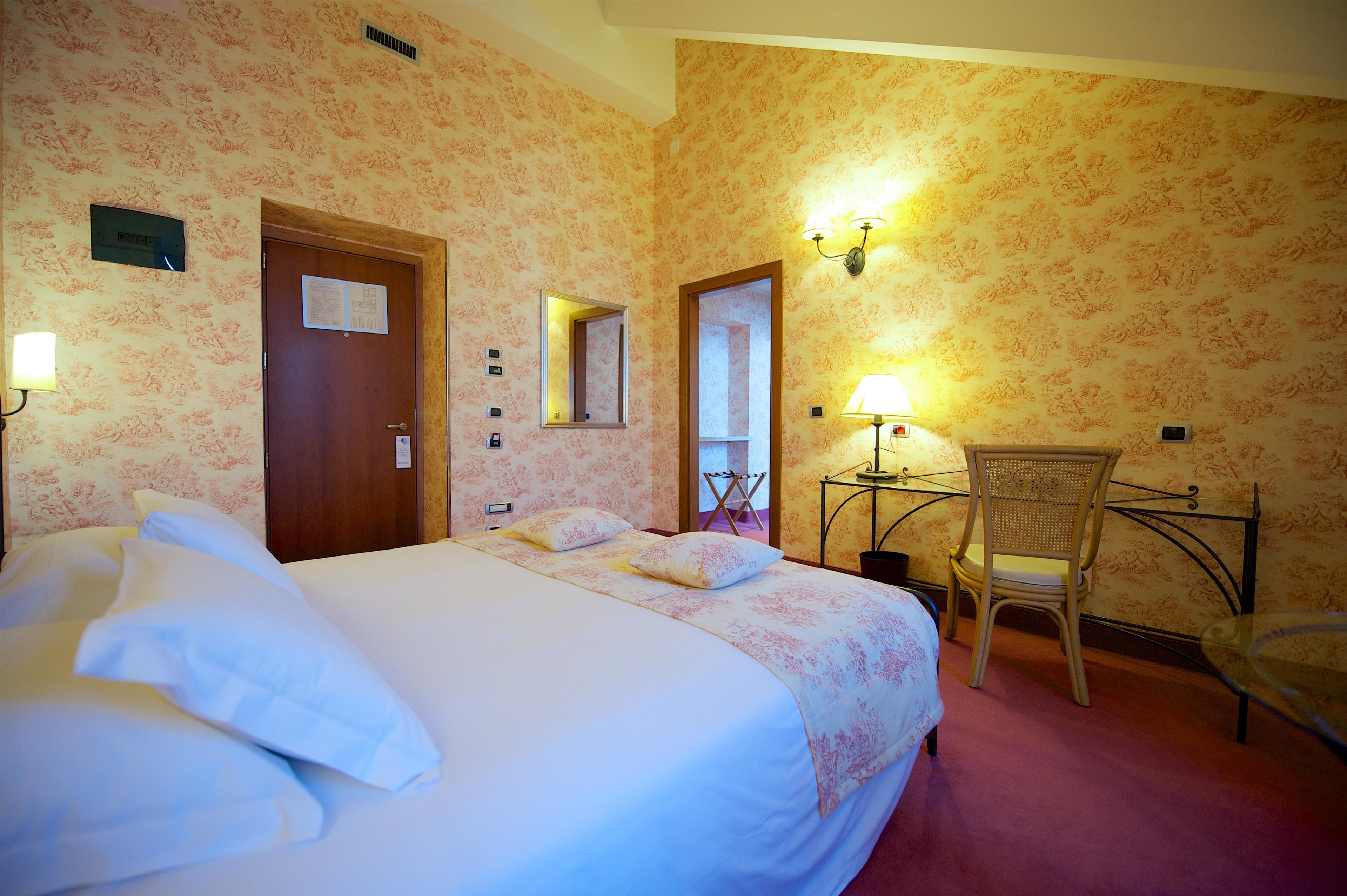 Una habitación de hotel con cama, una silla, un escritorio y un espejo.