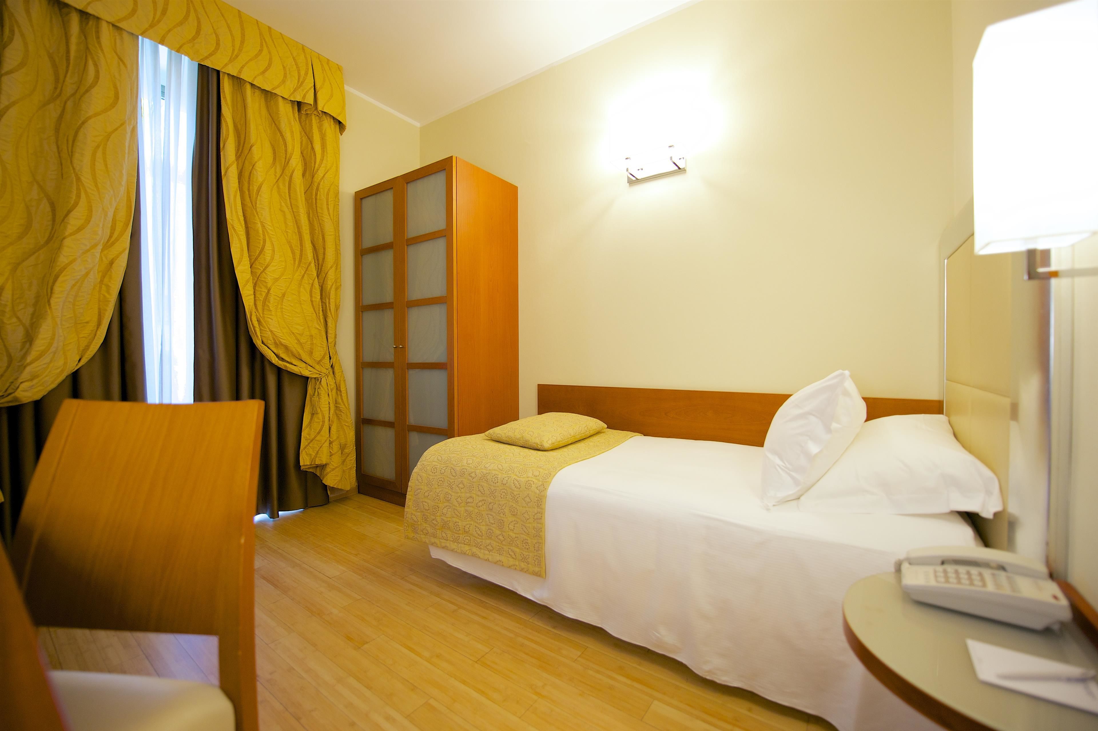 Een hotelkamer met een bed, een stoel, een bureau met telefoon en een kast.