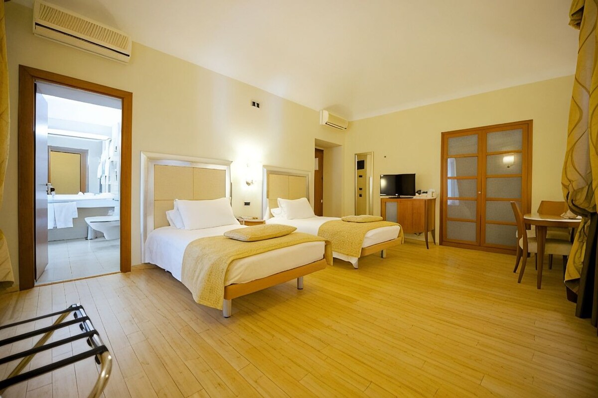 A hotel room with two beds, a desk, a chair, a television, and a bathroom visible through an open door.