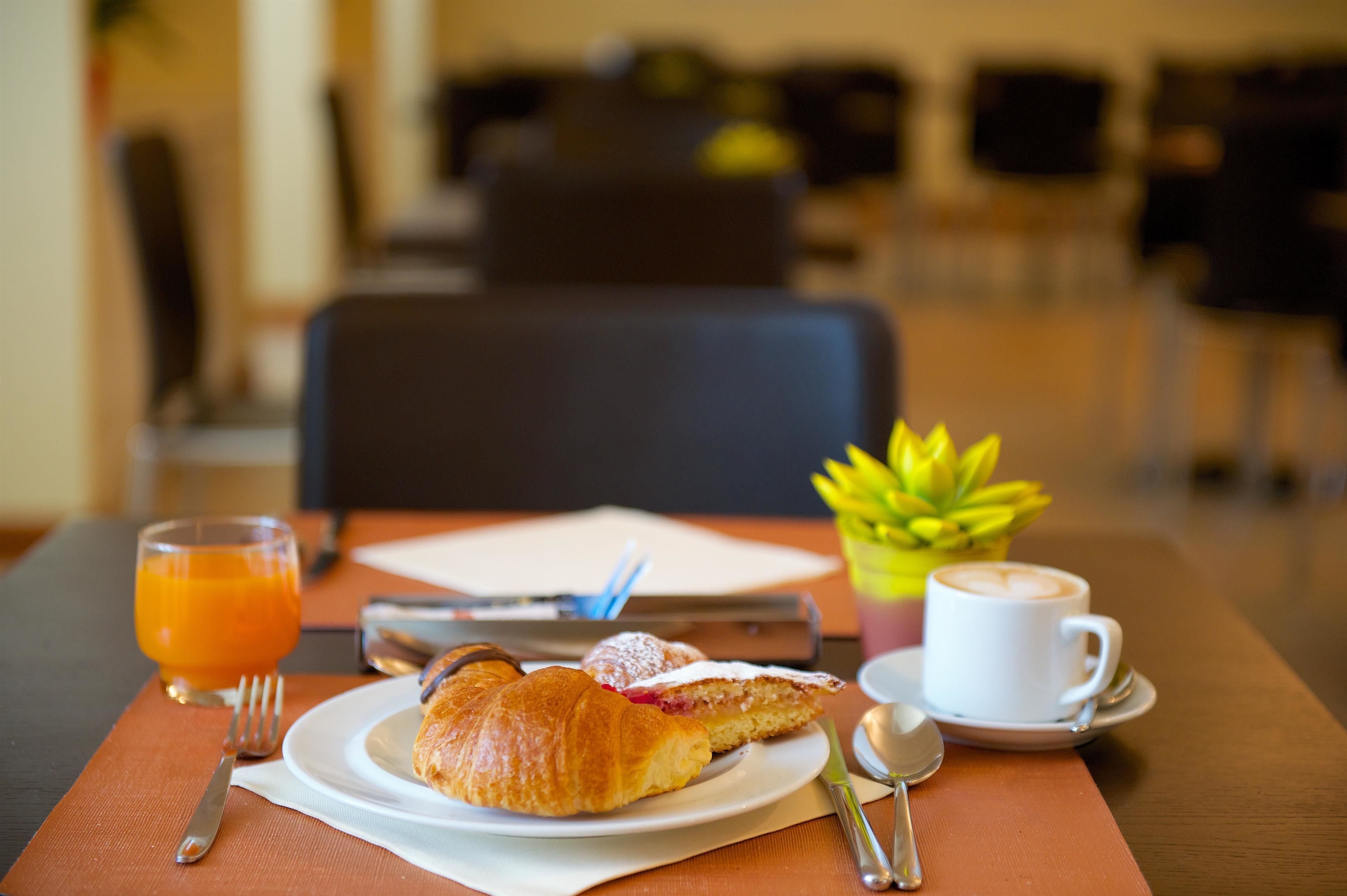 Un desayuno con croissants, una taza de café y un vaso de zumo de naranja sobre una mesa.