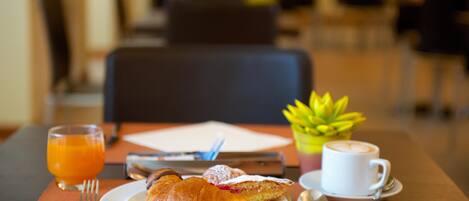 Un desayuno con croissants, una taza de café y un vaso de zumo de naranja sobre una mesa.