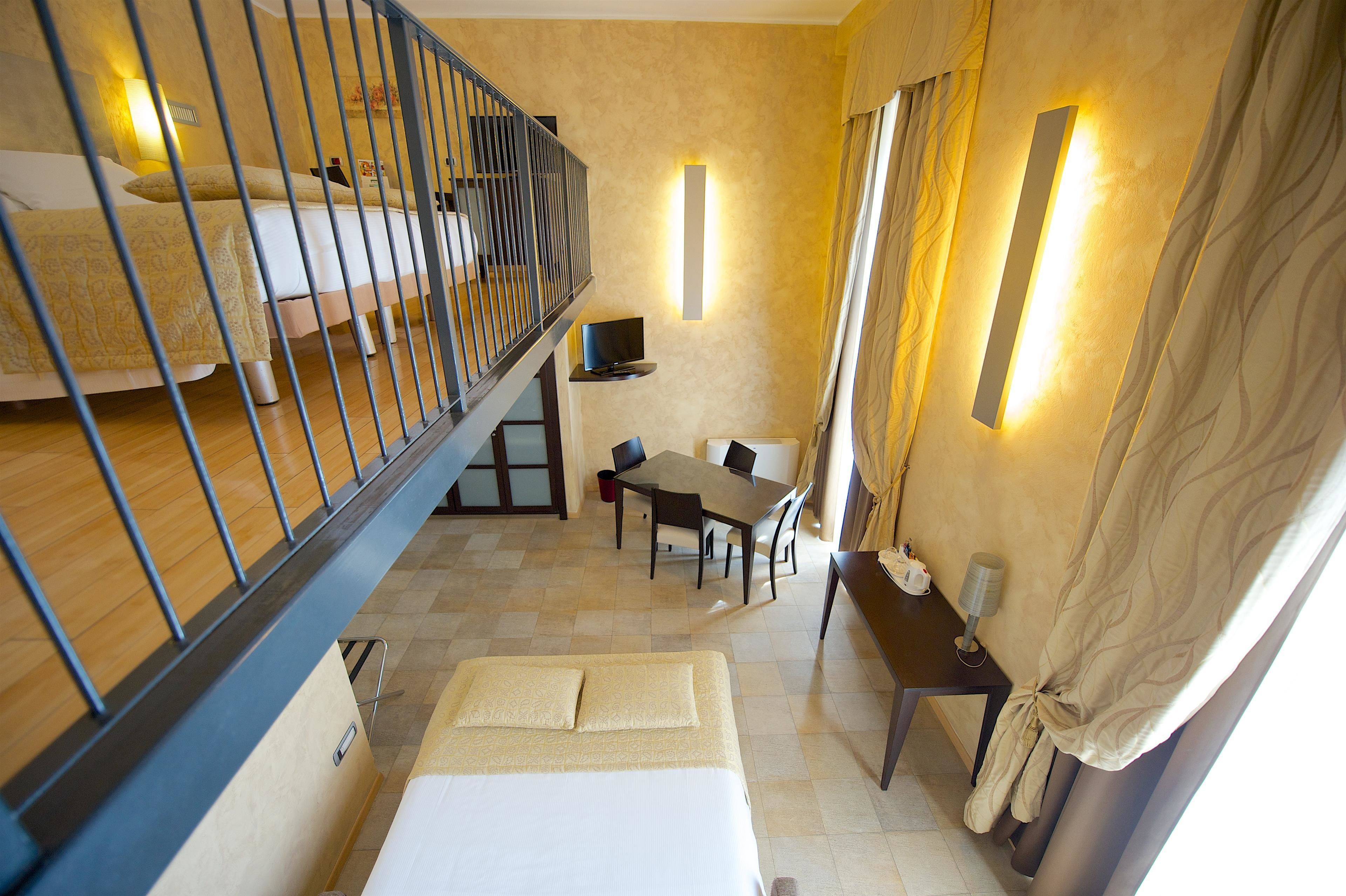 Habitación de hotel con balcón, zona de comedor y televisión.
