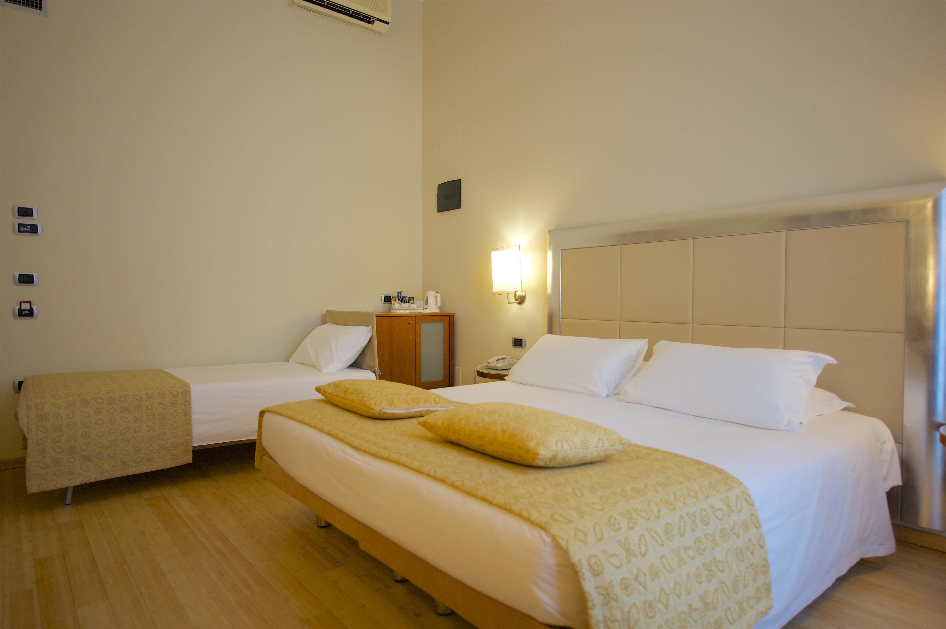 Una camera d'albergo con due letti, un comodino con lampada e una piccola credenza.