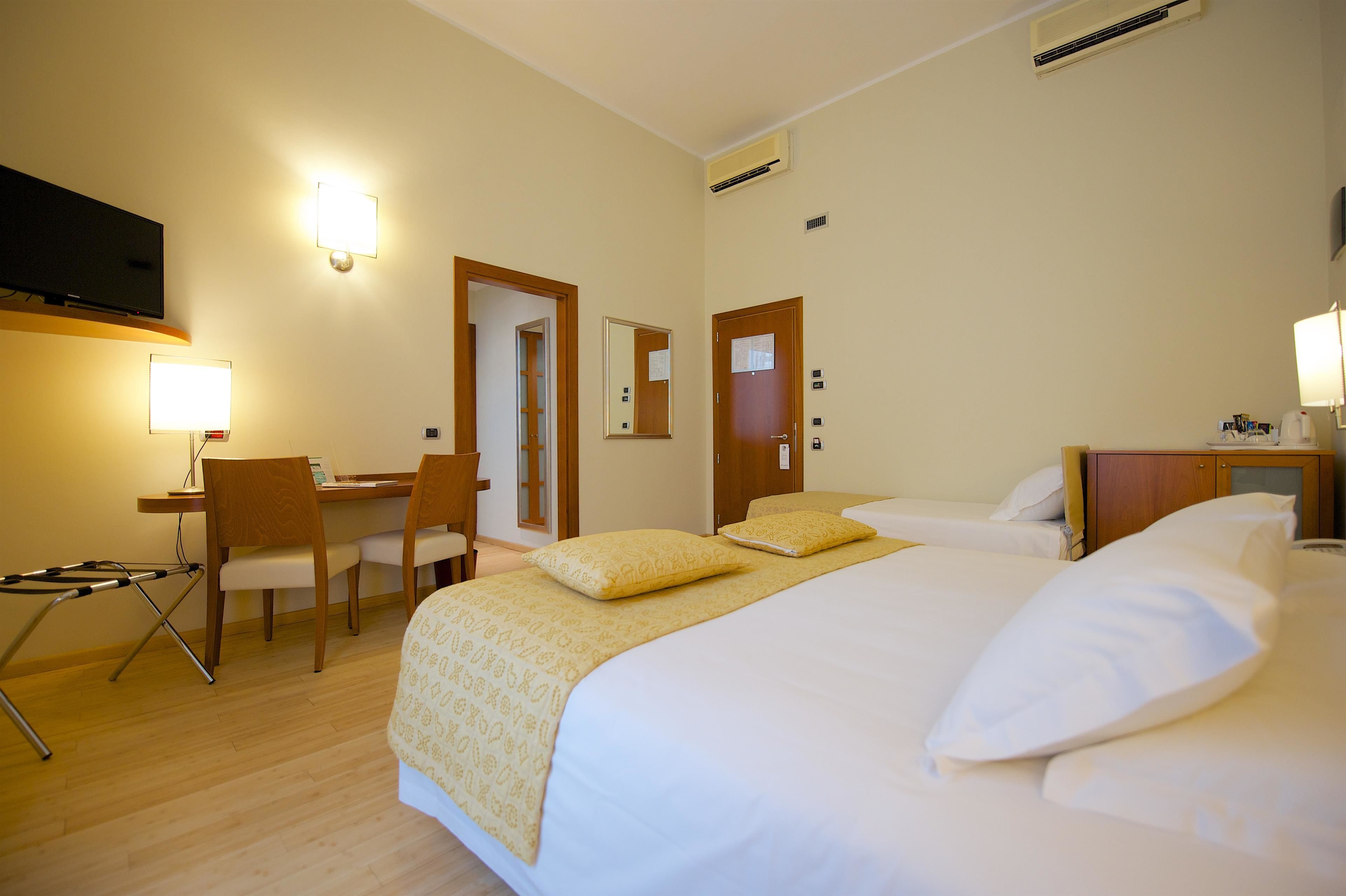 A hotel room with a bed, bedside table, chair, desk, and a flat-screen TV mounted on the wall.