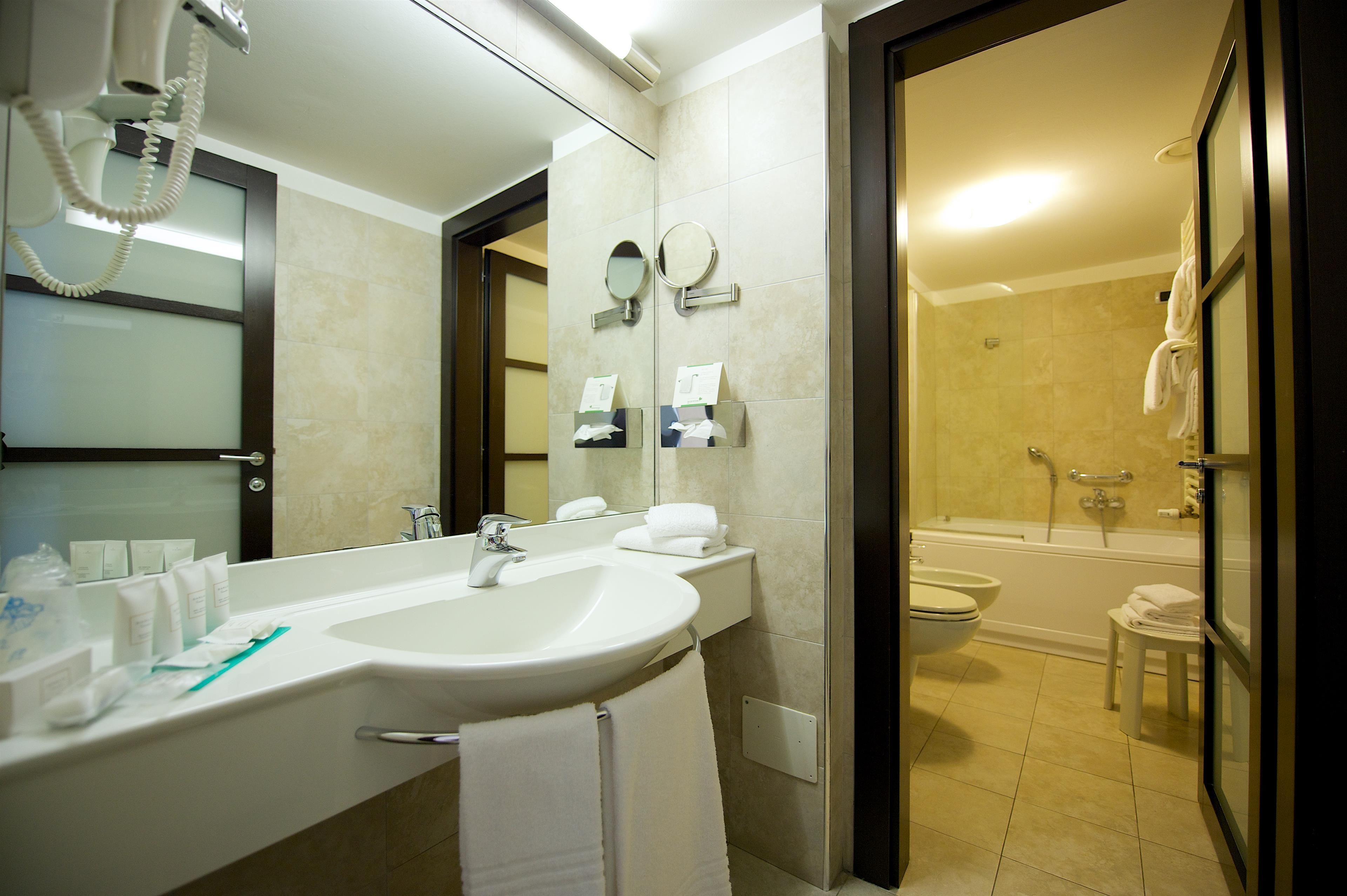 A modern bathroom with a sink, mirror, and toiletries. It includes a shower area with a bathtub and a toilet.