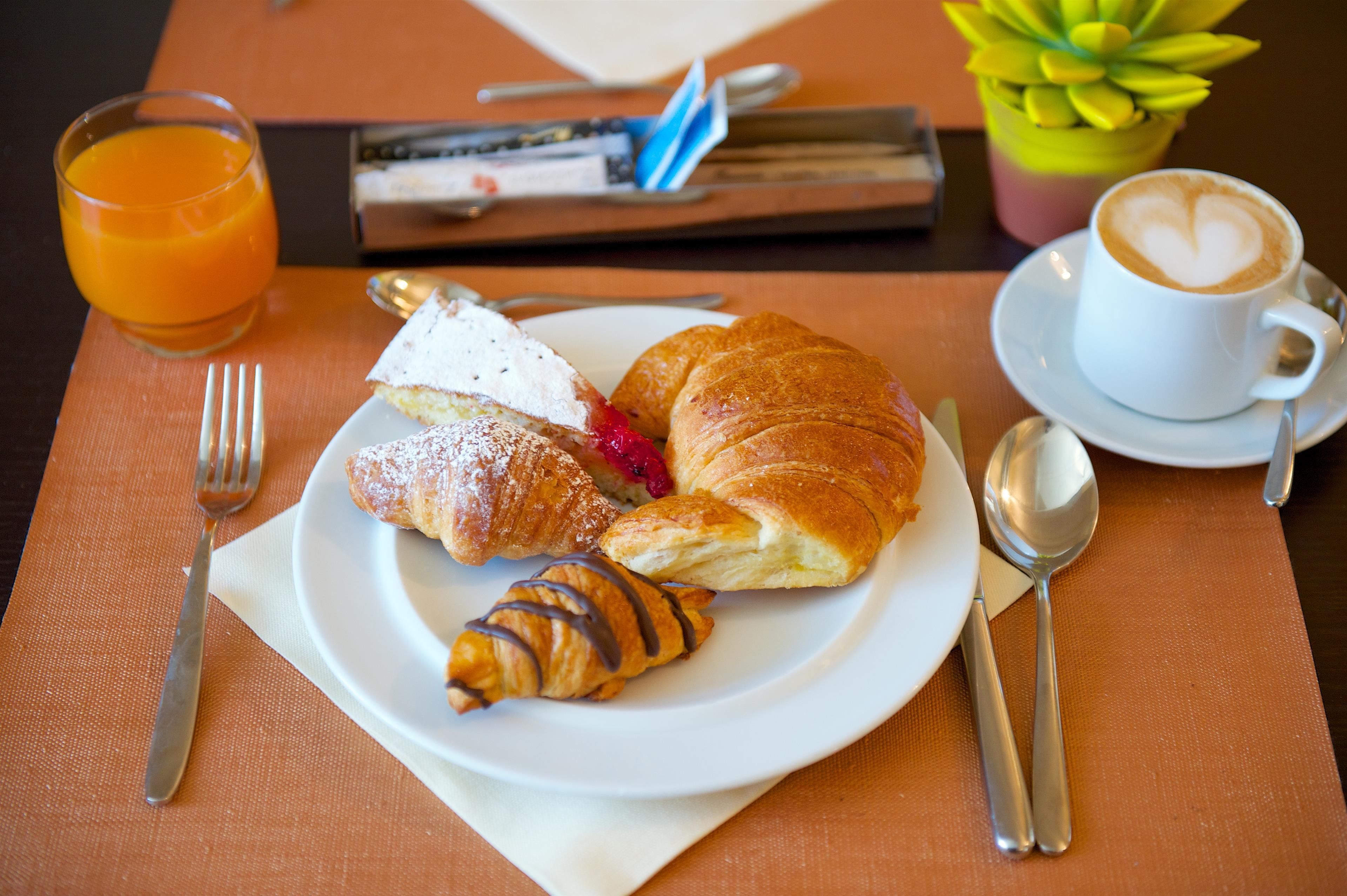 Colazione con croissant, una fetta di torta e una tazza di caffè su un tavolo.
