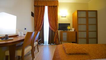 A hotel room with a bed, desk, chair, television, wardrobe, and curtains.