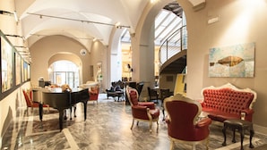 A spacious lobby with a grand piano, red upholstered chairs, and a marble floor.