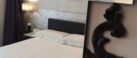 A hotel room with a bed, a nightstand, a lamp, and a decorative wall piece.