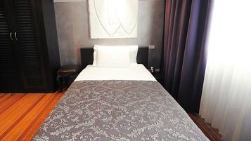 A hotel room with a large bed, a nightstand, a wall-mounted artwork, and a window with curtains.