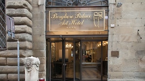 The exterior of Borgotese Palace Art Hotel with a stone facade and a glass entrance.