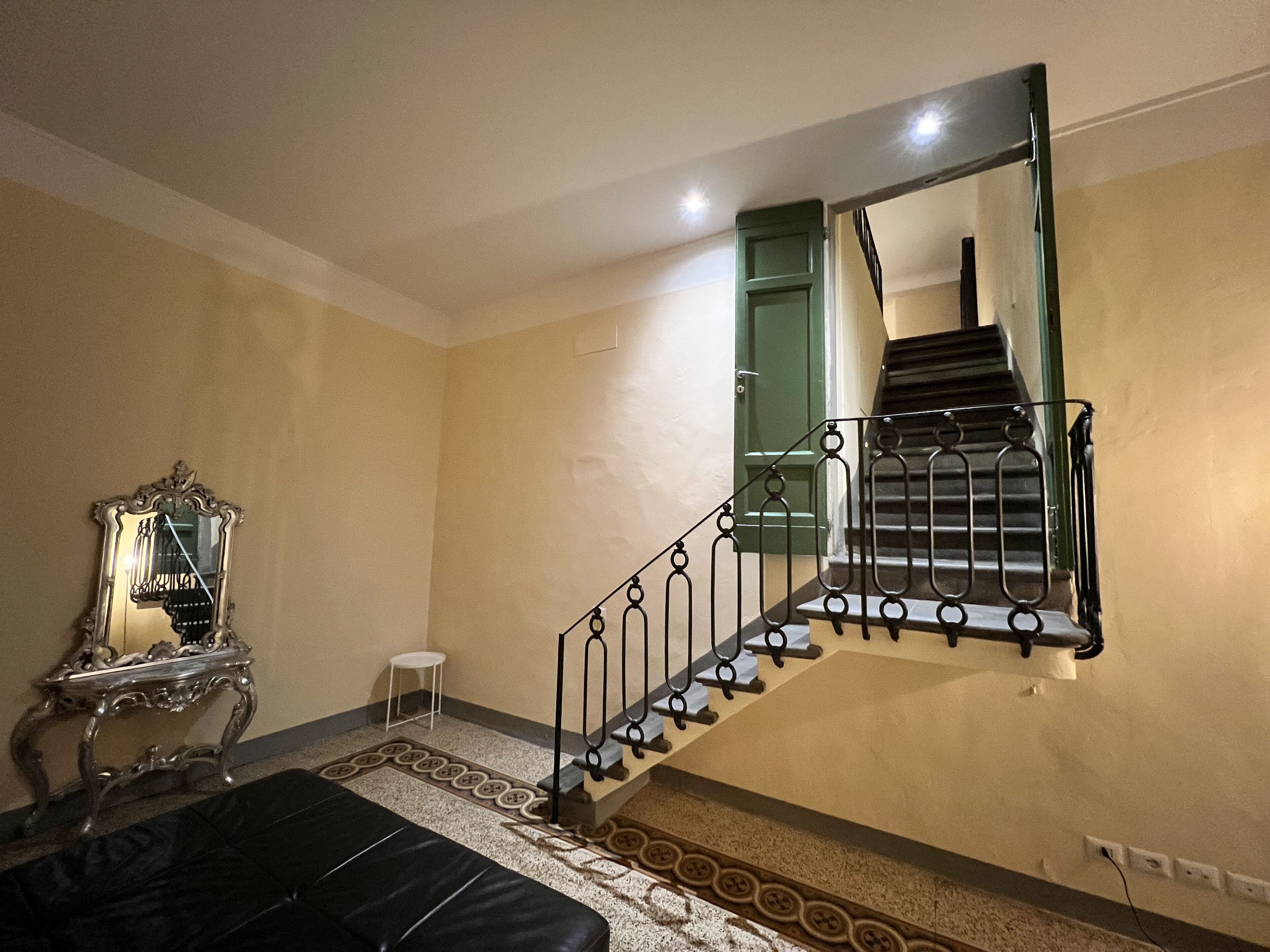 Une pièce avec un escalier, un miroir, une petite table et un tapis à motifs.