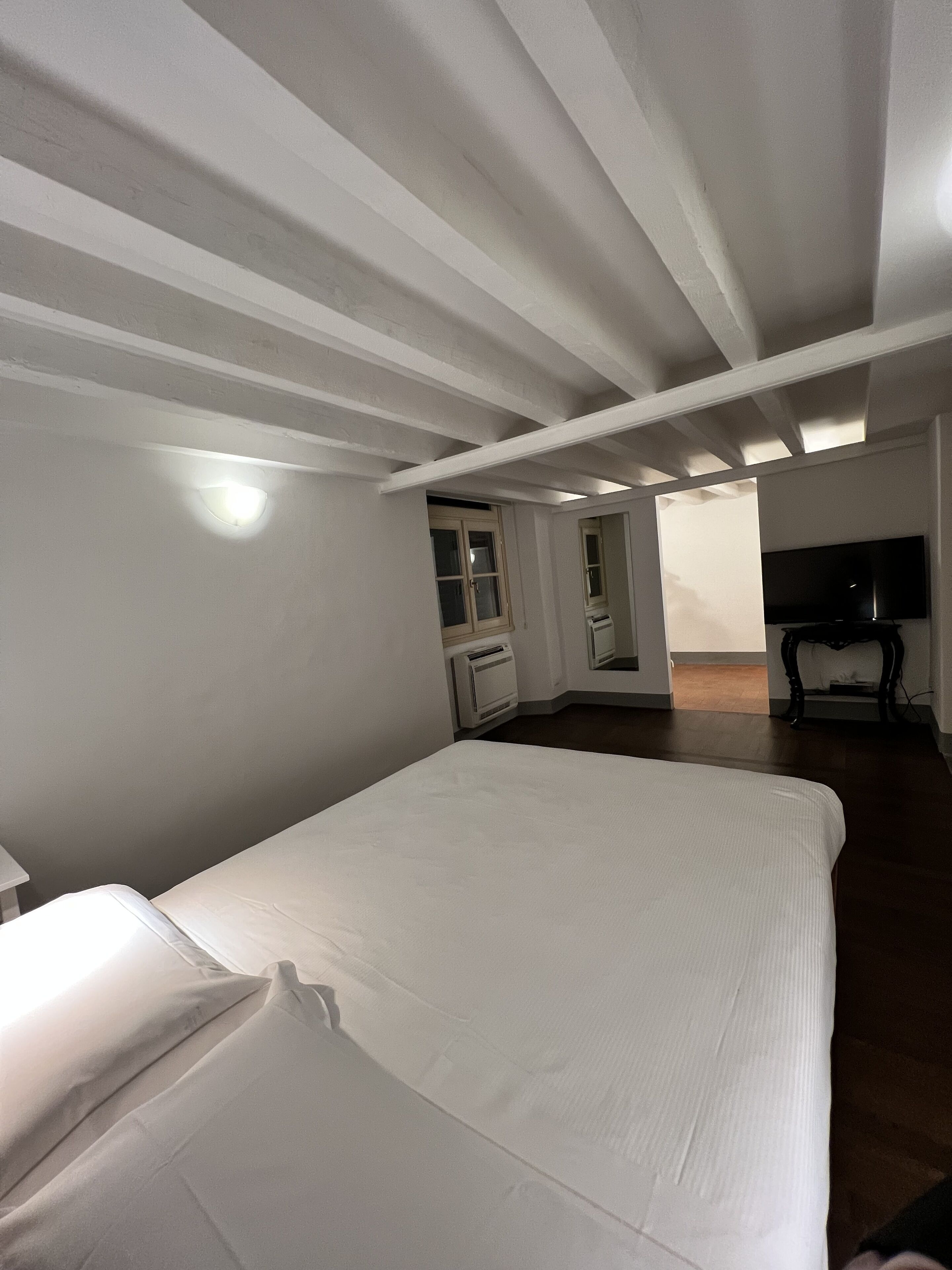 A bedroom with a bed, a window, a radiator, and a television.
