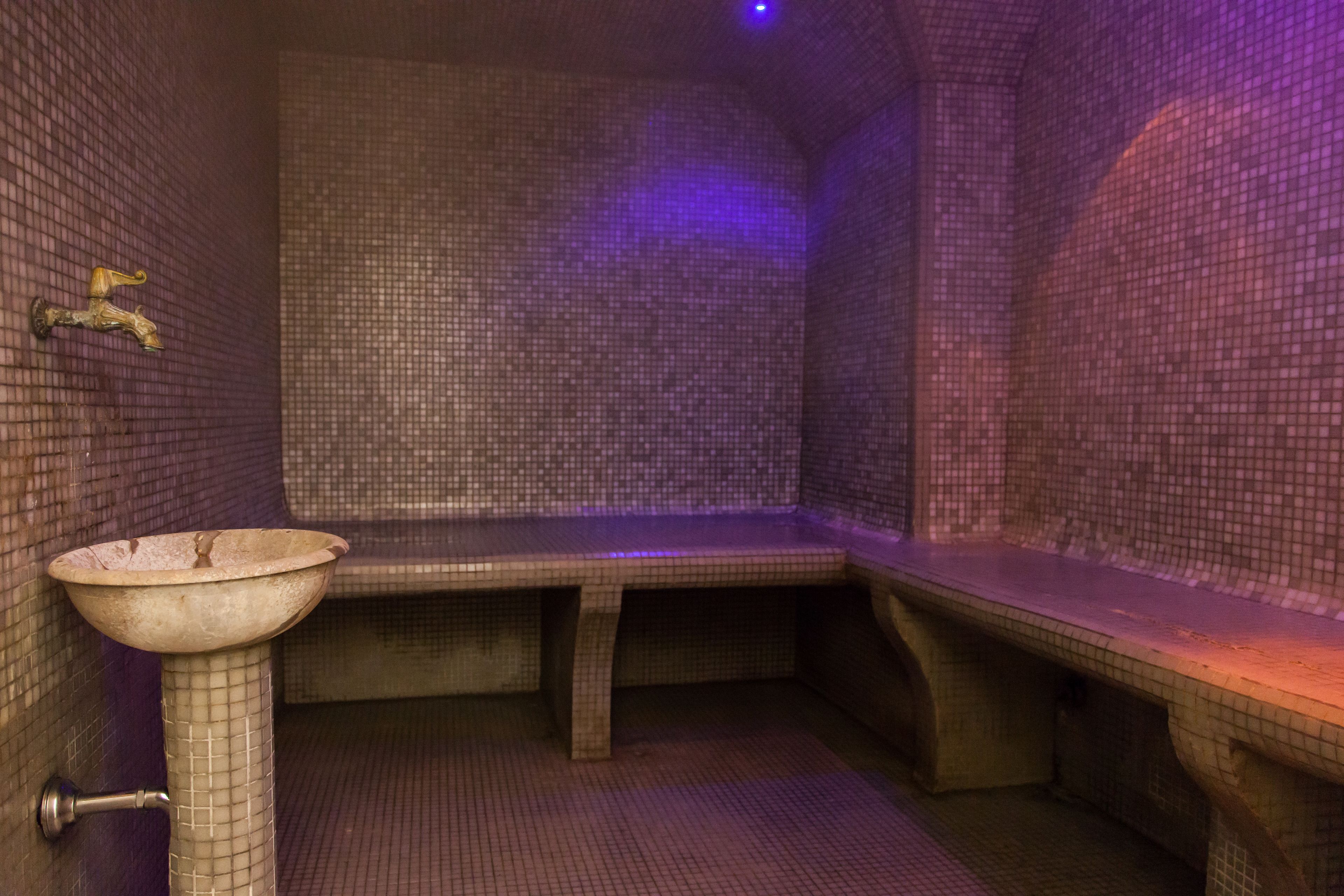 A small, tiled room with a bench and a sink.