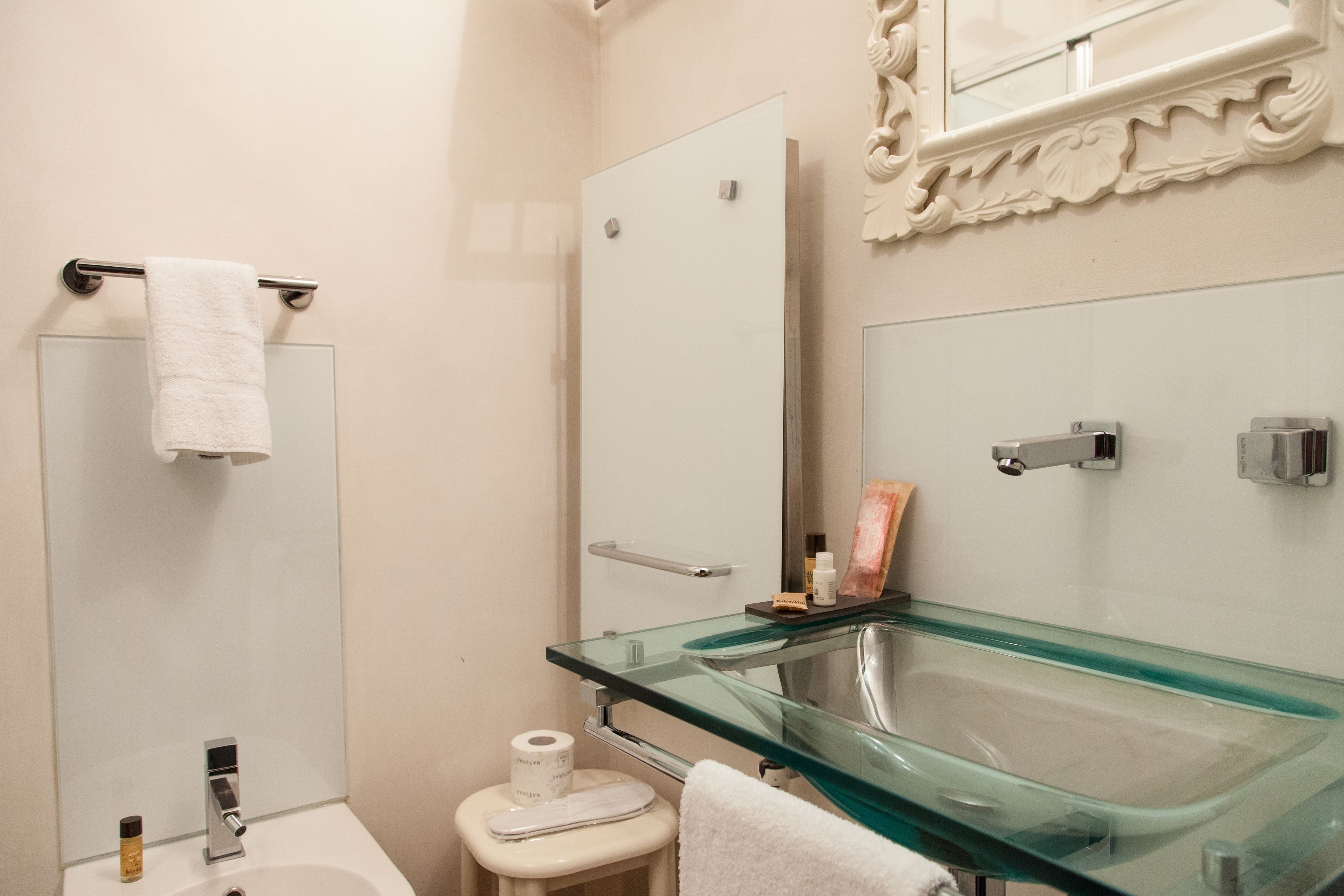 A bathroom with a glass sink, a toilet, a towel rack, and a door.