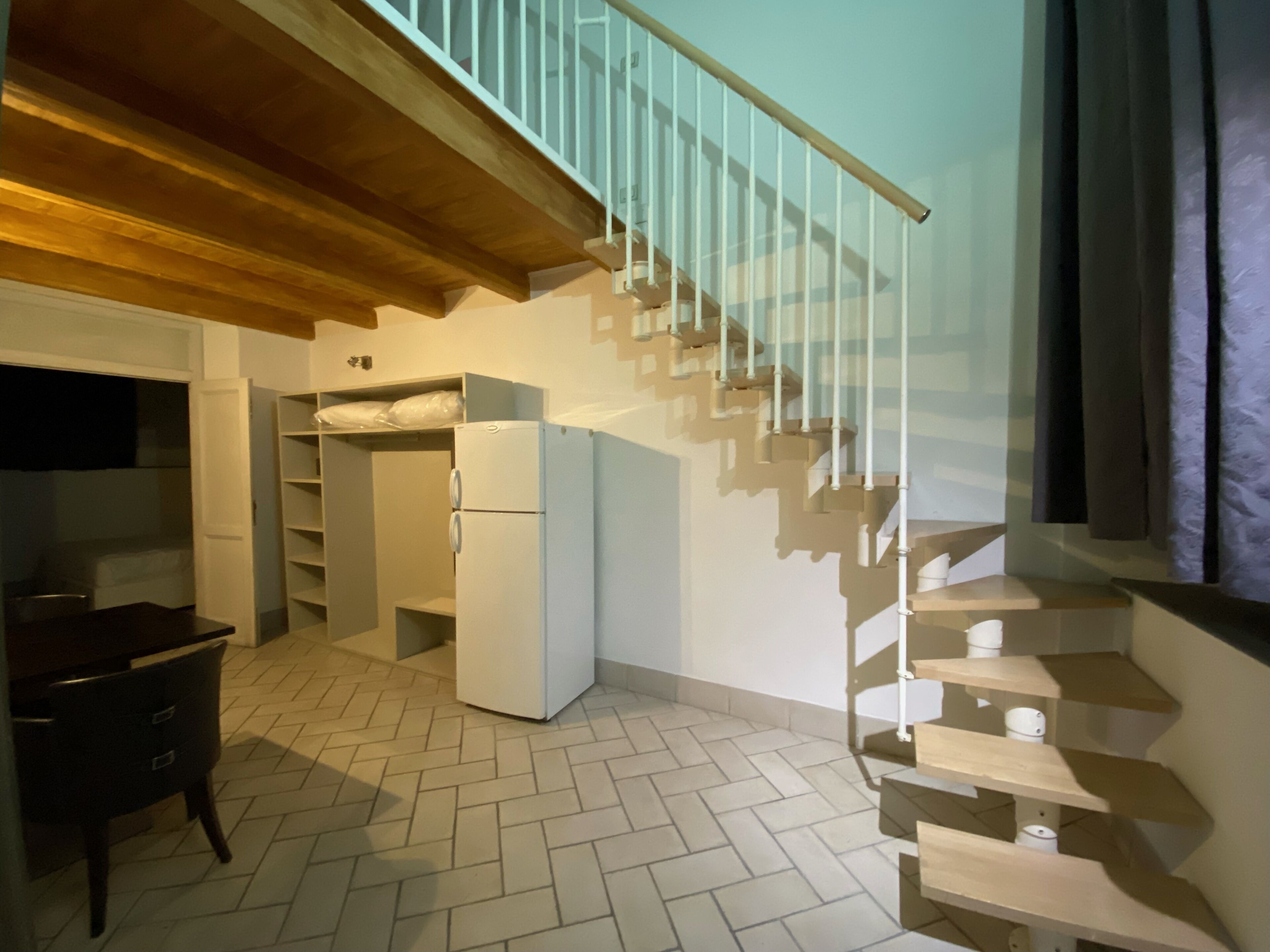 A compact kitchen with a built-in refrigerator, a wooden dining table, and a herringbone-patterned floor.