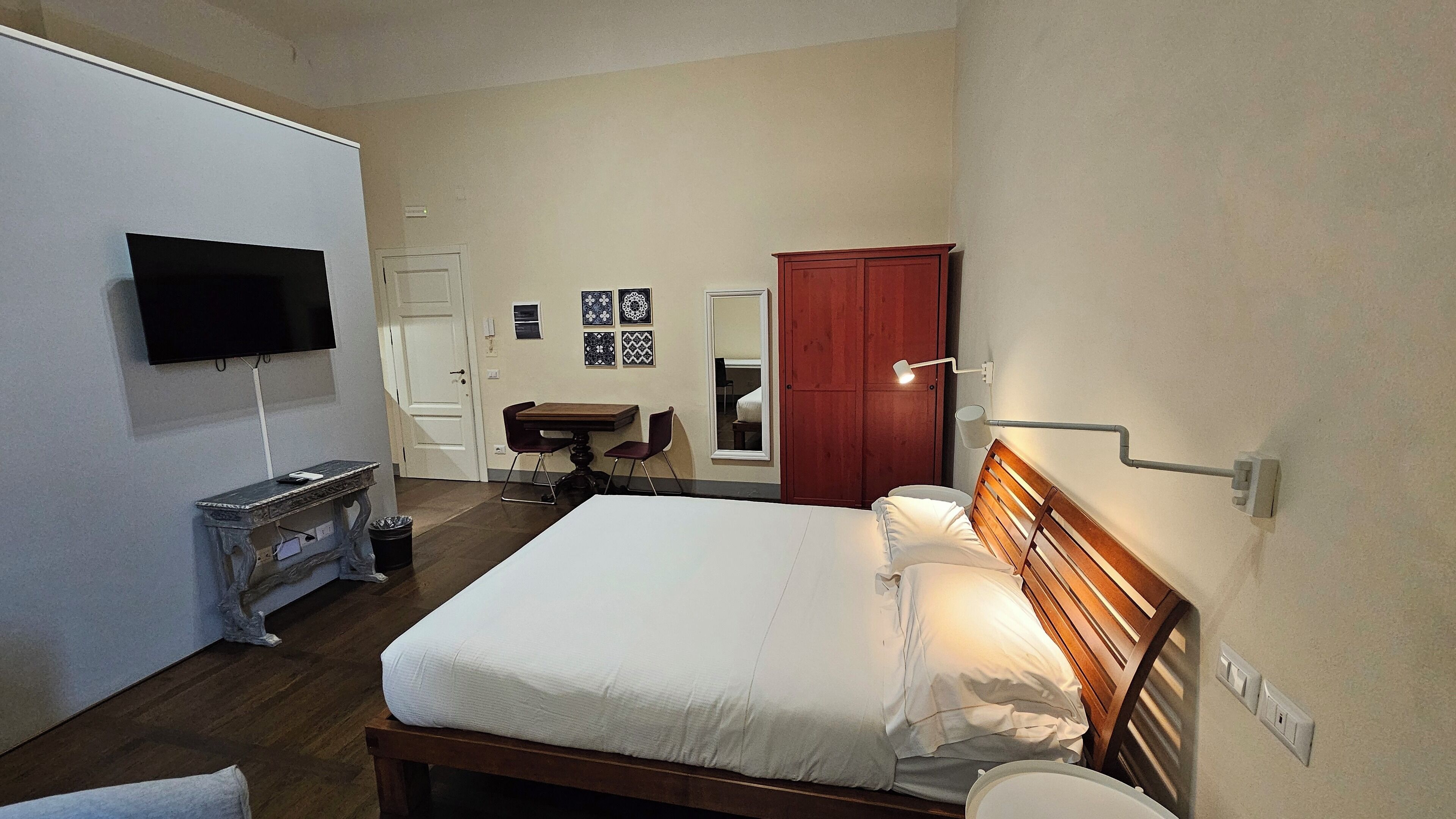 Una camera da letto con un letto, una scrivania, una sedia, una TV, un armadio e uno specchio.