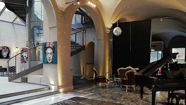 A spacious lobby with a grand piano, leather ottoman, and a staircase leading to upper floors.