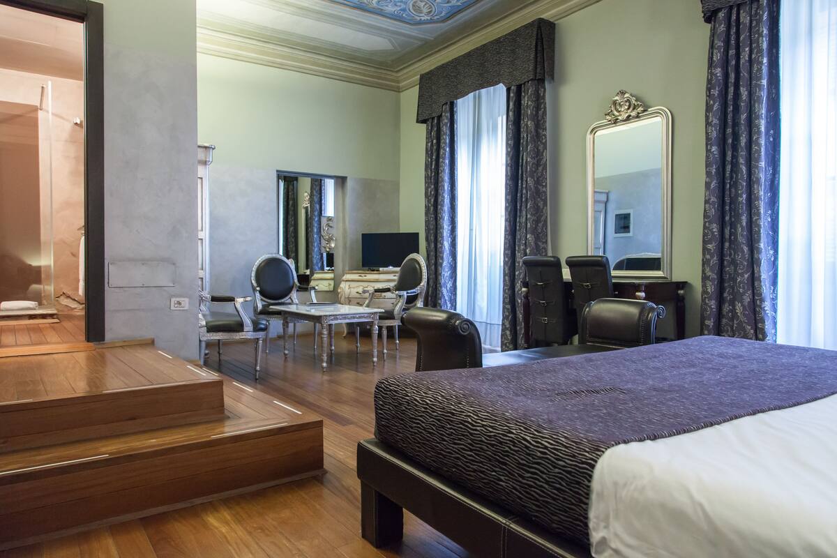 Een hotelkamer met een groot bed, een bureau met stoel, een klein tafeltje en een kledingkast.
